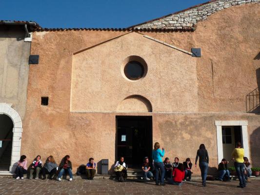 esterno antica chiesa ocra sconsacrata con fila di studenti seduti davanti