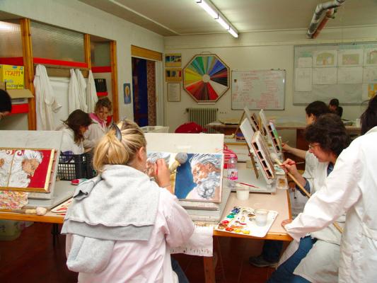 studenti con camici bianchi in aula intenti a dipingere mattoni, al muro due lavagne e ruota dei colori