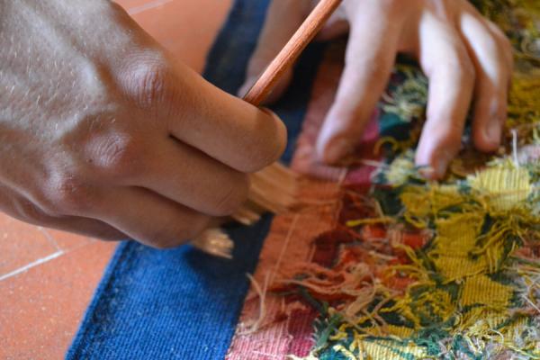 primo piano di mani con pennello che lavorano un tappeto