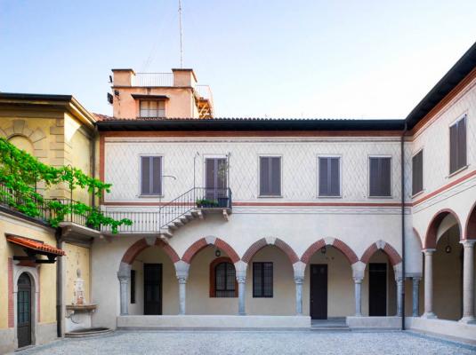 cortile interno di un edificio medievale bianco con portici con inserti rossi e pianta